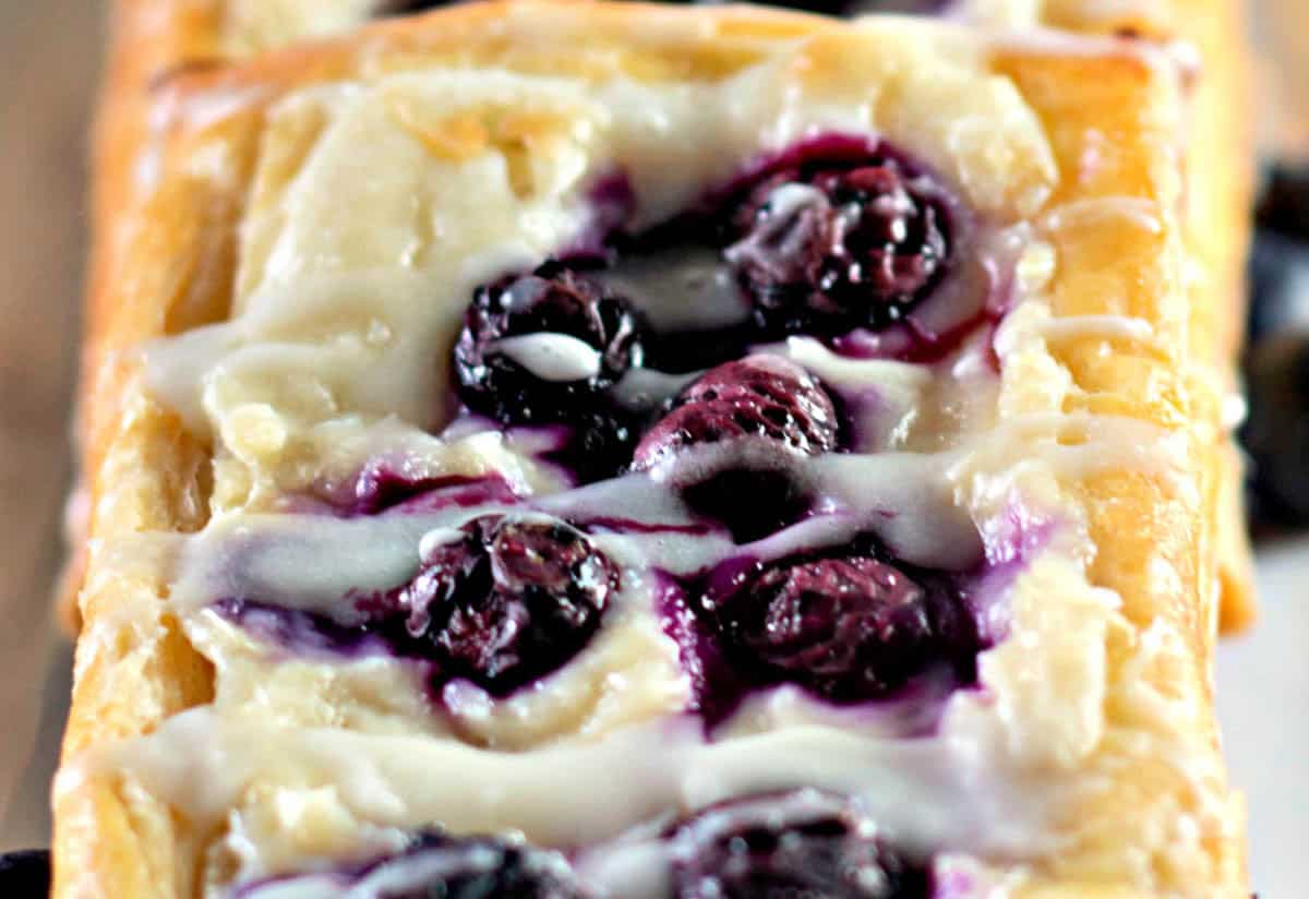 Blueberry Danishes with white icing rest invitingly on a baking tray, showcasing their perfect rectangular shape.