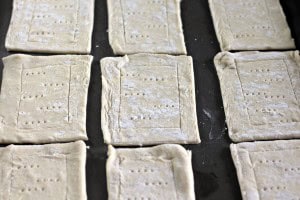 Rectangular pieces of raw pastry dough with fork pricks, perfect for making delicious blueberry Danishes, are arranged on a baking sheet.