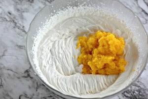 A bowl of whipped cream mixed with a mound of mashed yellow fruit rests on a marble countertop, reminiscent of the creamy texture found in a Boston Cream Pie Cookie.