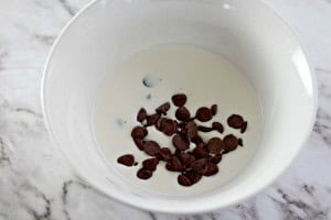 A white bowl containing milk and chocolate chips sits invitingly on a marble surface, reminiscent of the sweet allure of a Boston Cream Pie Cookie.