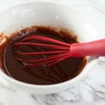 A bowl with chocolate mixture and a red whisk sits on a marble countertop, ready to transform simple ingredients into delightful Boston Cream Pie Cookies.