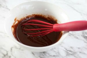 A bowl with chocolate mixture and a red whisk sits on a marble countertop, ready to transform simple ingredients into delightful Boston Cream Pie Cookies.