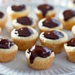 A plate of mini Boston Cream Pie Cookies topped with chocolate glaze, elegantly arranged in rows on a white platter.