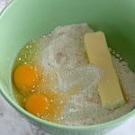 A green bowl contains two raw eggs, flour, and a stick of butter on a marble surface&mdash;the perfect start to whipping up a batch of Boston Cream Pie Cookies.