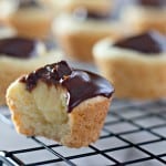 Mini cupcakes with chocolate topping on a cooling rack, reminiscent of a delightful Boston Cream Pie Cookie, with one having a bite taken out.