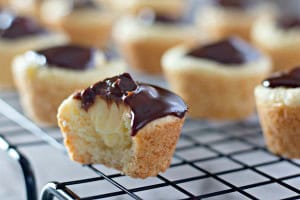 Mini cupcakes with chocolate topping on a cooling rack, reminiscent of a delightful Boston Cream Pie Cookie, with one having a bite taken out.