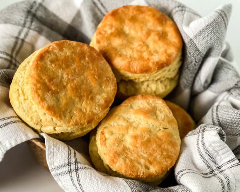 A basket of golden-brown biscuits resting on a plaid cloth, showcasing the perfect result of cherished biscuit recipes.