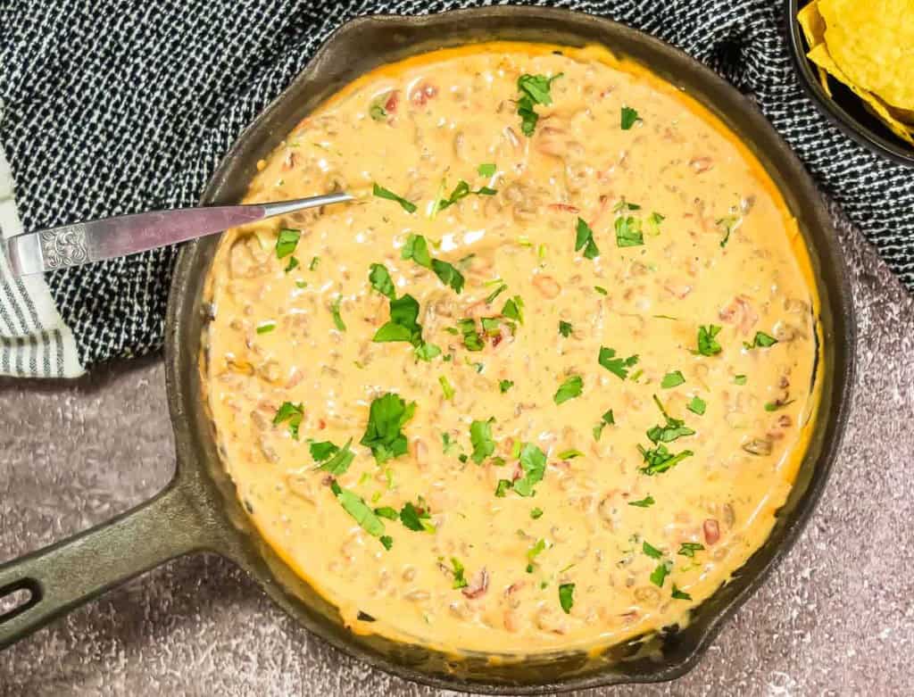 A skillet filled with creamy cheese dip topped with chopped green herbs. A spoon rests in the skillet.