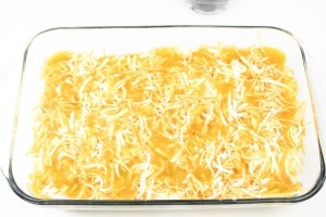 A glass baking dish filled with uncooked shredded cheese and a yellow sauce.