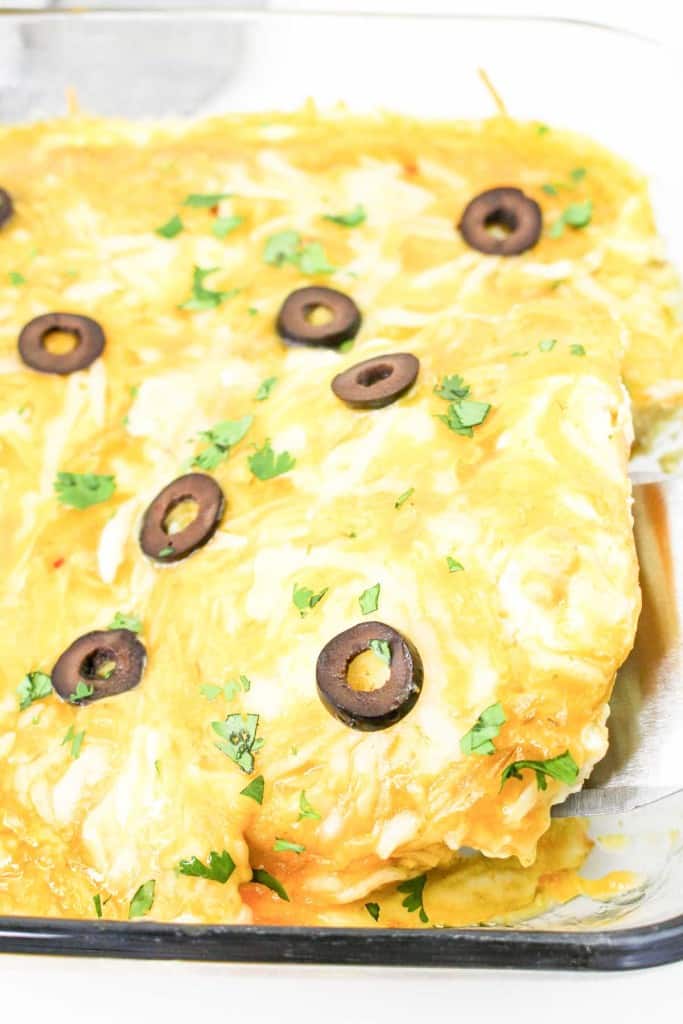 A baked dish topped with melted cheese, sliced black olives, and chopped herbs in a clear glass baking dish, partially cut into squares.