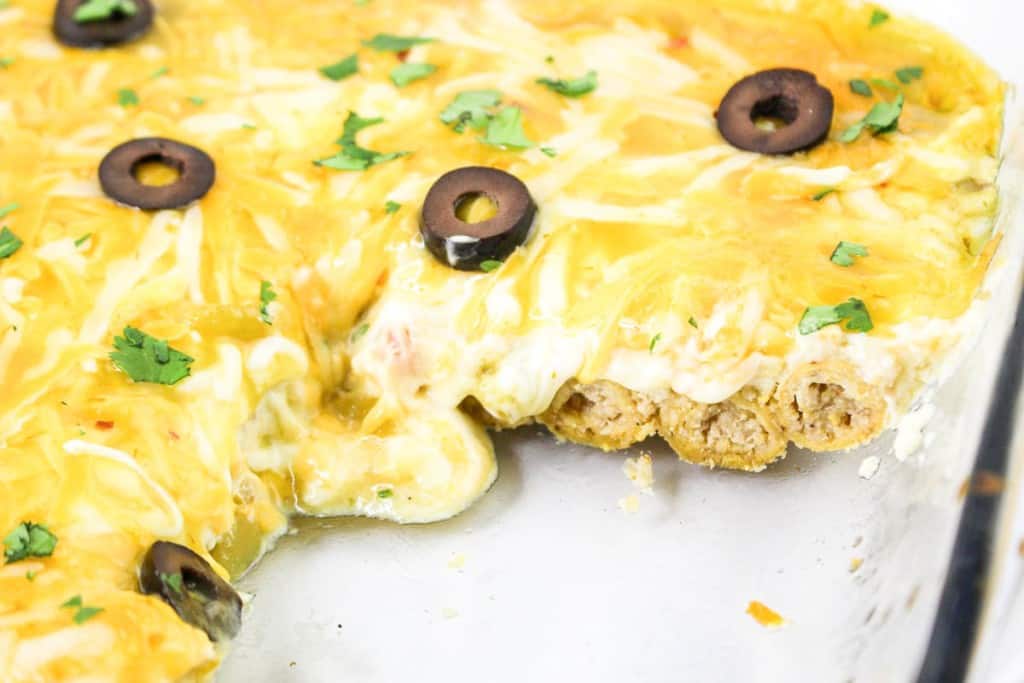 Close-up of a partially eaten casserole with melted cheese, black olive slices, and chopped cilantro on top. Visible layers include meat and a creamy sauce.