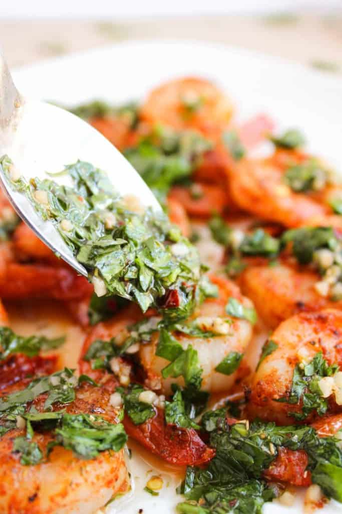 Close-up of cooked shrimp topped with a mixture of herbs and garlic being spooned onto a plate, perfect for a quick dinner.