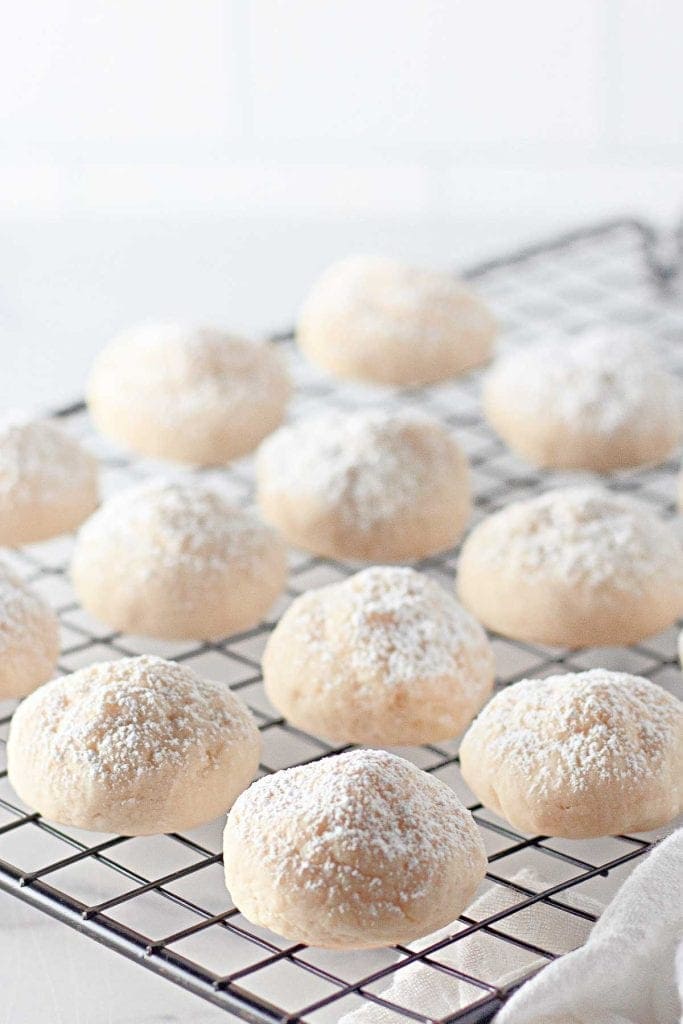 Round cookies dusted with powdered sugar cooling on a wire rack.