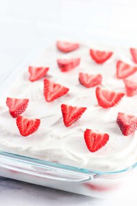 Glass dish with a delightful whipped cream-topped dessert, adorned with sliced strawberries, reminiscent of a luscious strawberry ice cream cake.
