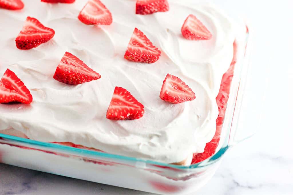 A rectangular glass dish showcases a delightful strawberry ice cream cake, adorned with whipped cream and sliced strawberries, creating a tempting treat perfect for any occasion.