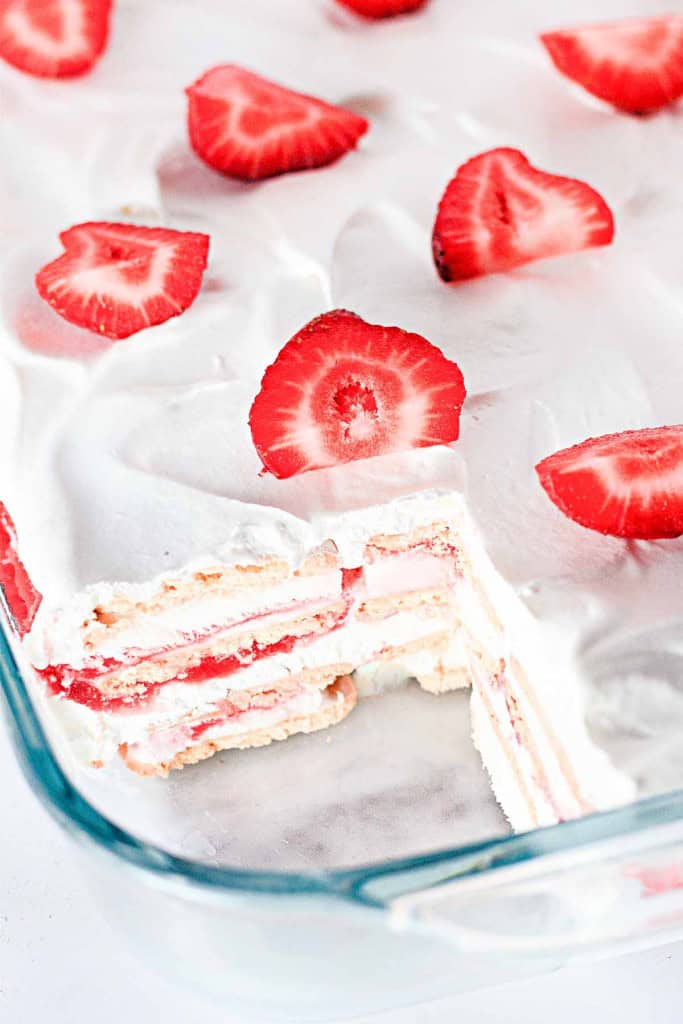 A decadent layered dessert featuring whipped cream and strawberry slices in a glass dish, reminiscent of a sumptuous strawberry ice cream cake, with a slice removed to reveal its intricate layers.