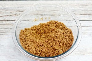 A glass bowl filled with brown sugar on a wooden surface.