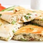Grilled quesadillas filled with chicken, veggies, and garnished with cilantro, served on a white plate.