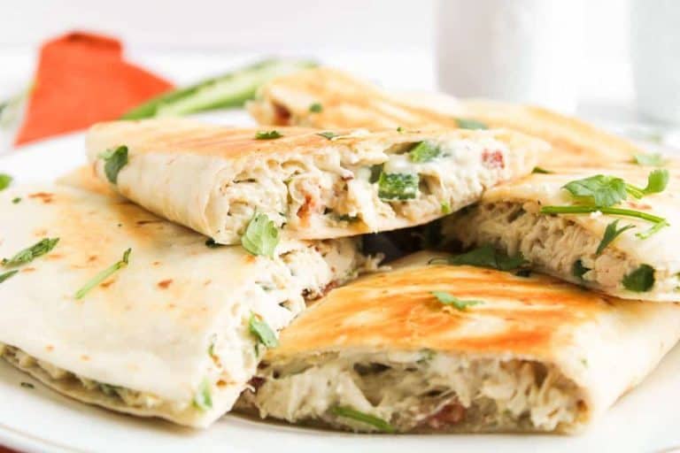 Grilled quesadillas filled with chicken, veggies, and garnished with cilantro, served on a white plate.