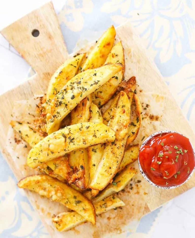 Crispy potato wedges topped with herbs and cheese on a wooden board, served with a side of ketchup.