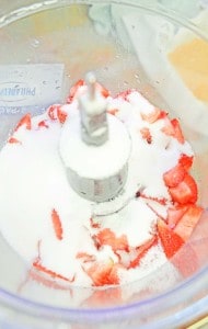 Sliced strawberries with sugar in a food processor bowl, ready for blending.