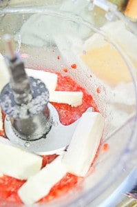 Food processor blending chopped cream cheese with strawberries.