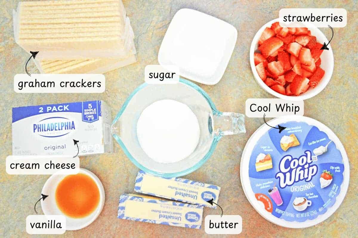 Ingredients laid out for Strawberry Cheesecake Bars: graham crackers, cream cheese, sugar, vanilla, butter, Cool Whip, and sliced strawberries in separate containers.