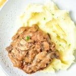 A plate with mashed potatoes topped with a rich brown mushroom and onion gravy, perfectly complementing the succulent Turkey Salisbury Steak.