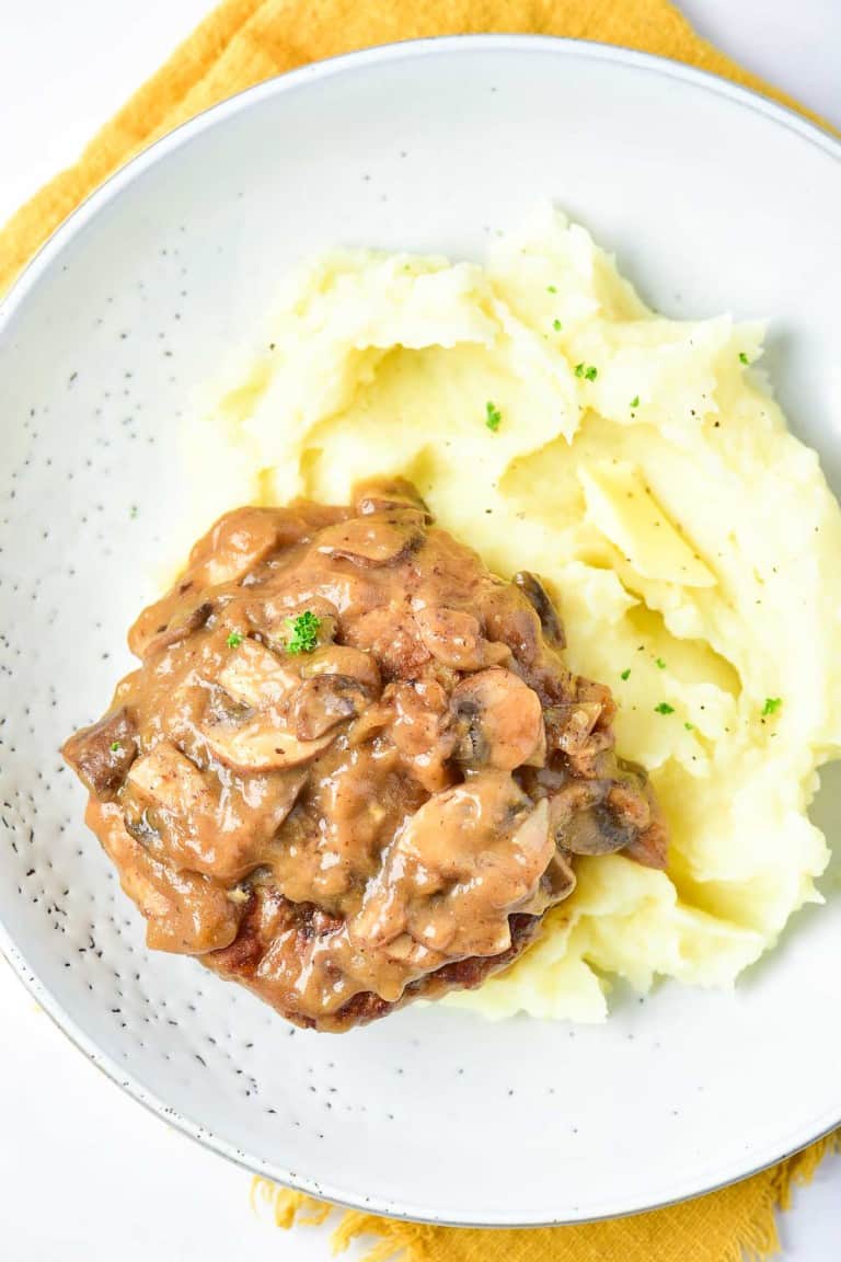 A plate with mashed potatoes topped with a rich brown mushroom and onion gravy, perfectly complementing the succulent Turkey Salisbury Steak.
