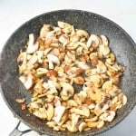 Chopped mushrooms dance in a black frying pan on a light surface, releasing aromas that perfectly complement the rich flavors of Turkey Salisbury Steak.