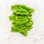 Halved green peppers arranged on white parchment paper, viewed from above.