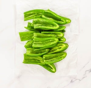 Halved green peppers arranged on white parchment paper, viewed from above.