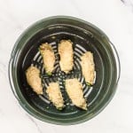 Seven breaded jalapeño poppers are arranged in a circular air fryer basket, placed on a marble-effect surface.