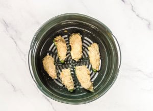 Seven breaded jalapeño poppers are arranged in a circular air fryer basket, placed on a marble-effect surface.