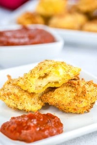 Breaded, fried ravioli on a white plate with marinara sauce, one ravioli is cut open to show filling.