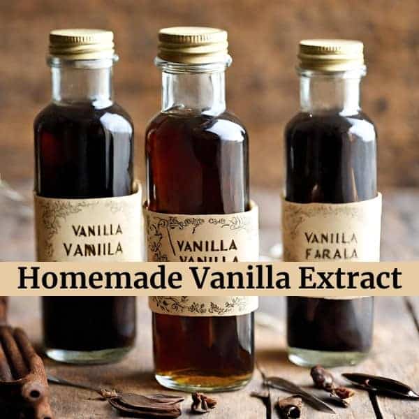 Three bottles of homemade vanilla extract with vintage labels on a wooden surface, surrounded by vanilla pods and cinnamon sticks.