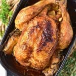 Roasted whole chicken in a baking dish, seasoned with herbs and garnished with rosemary sprigs, on a woven placemat.