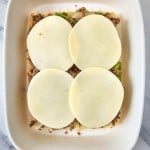 Shallow dish with a layer of bread topped with chopped ingredients, four slices of cheese, ready for baking.