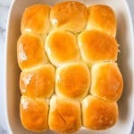 A baking dish with twelve golden brown dinner rolls, brushed with butter, on a marble surface.