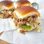 Three pulled pork sliders with shredded meat, green peppers, and onions on white paper.