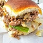 Close-up of a sandwich with shredded meat, sliced onions, and green peppers in a soft bun.