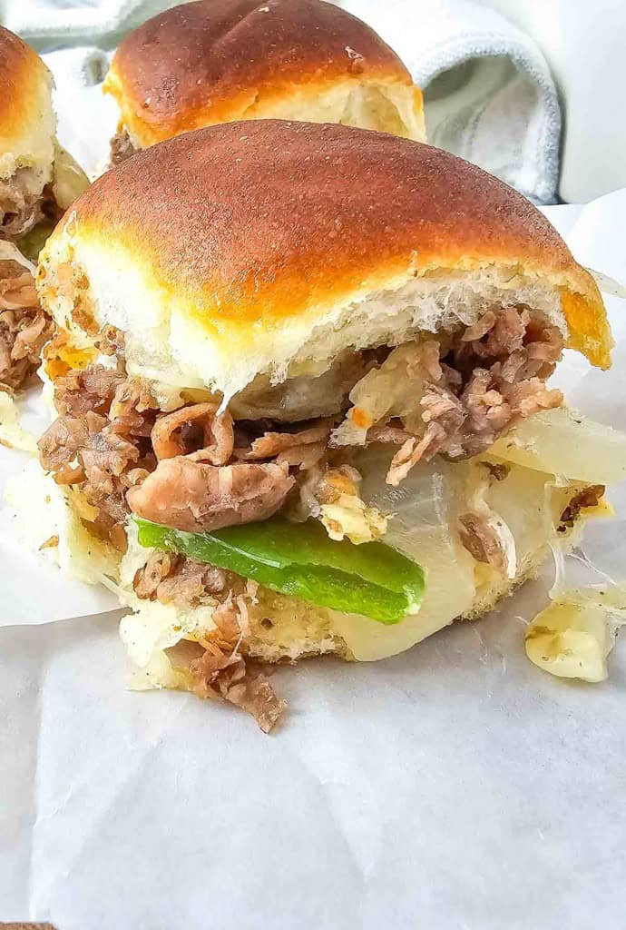 Close-up of a sandwich with shredded meat, sliced onions, and green peppers in a soft bun.