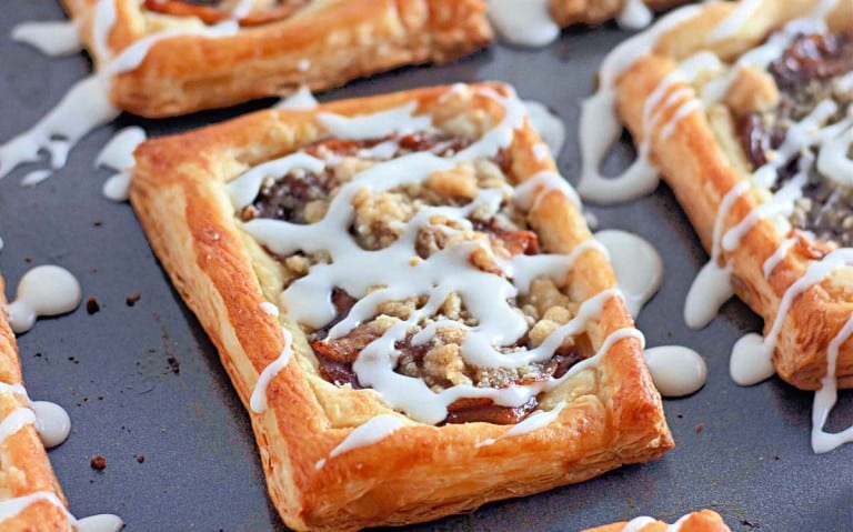 Rectangular apple crumb danishes topped with icing and crumble sit on a baking sheet.