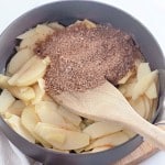 Sliced apples in a pan with brown sugar and spices, reminiscent of an apple crumb Danish, being stirred with a wooden spatula.