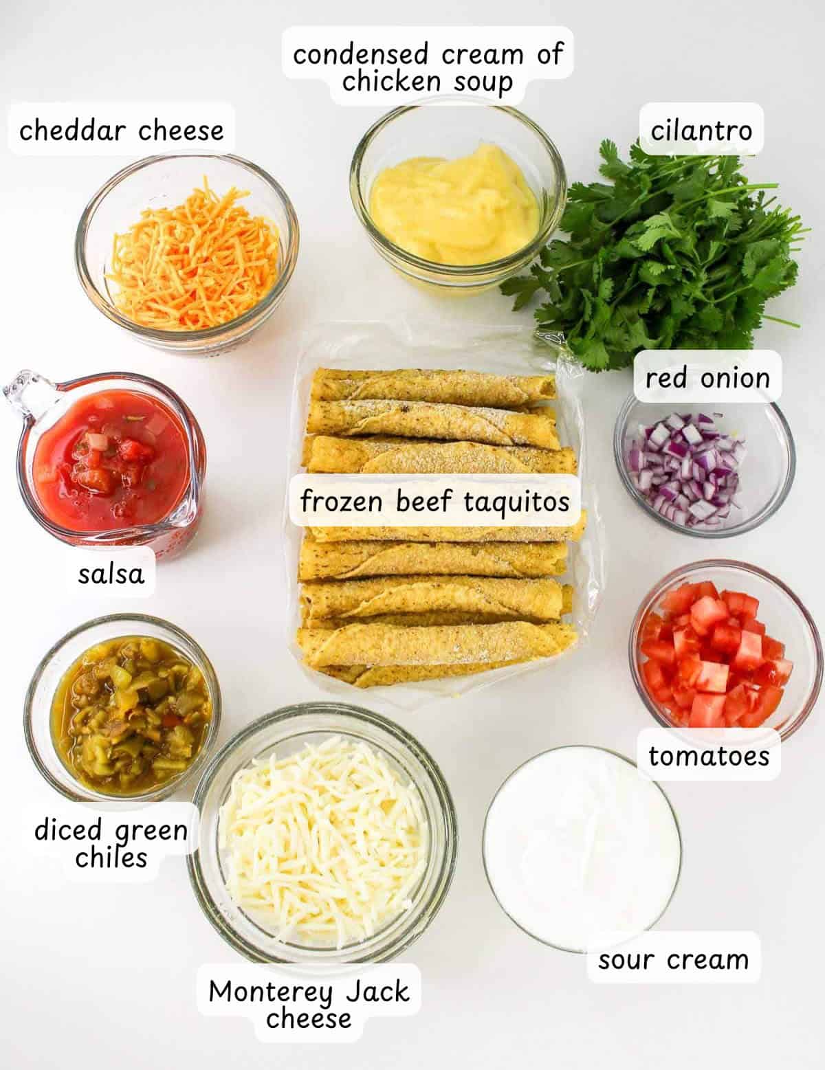 Frozen beef taquitos surrounded by bowls of cheddar cheese, salsa, diced green chiles, and more—everything you need to create a delicious beef taquito casserole for your next meal.