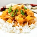 A plate of white rice topped with Crock Pot Hawaiian Chicken stew, featuring diced meat, yellow vegetables, and a garnish of sliced green onions.