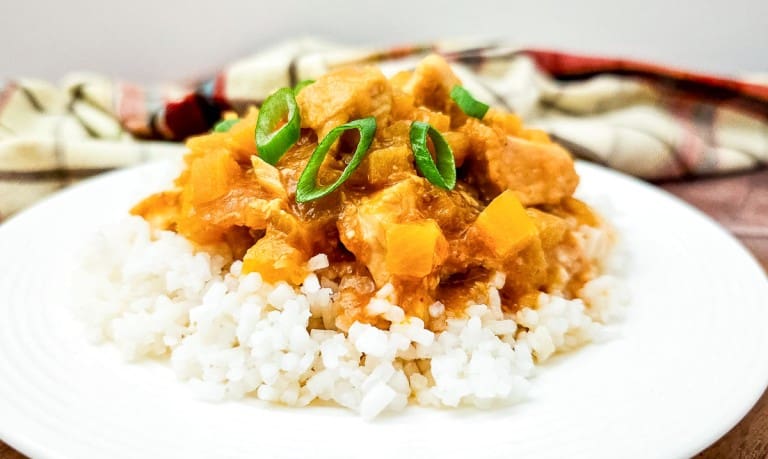 A plate of white rice topped with Crock Pot Hawaiian Chicken stew, featuring diced meat, yellow vegetables, and a garnish of sliced green onions.