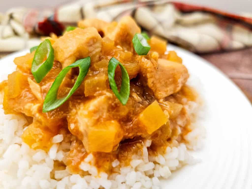 A plate of white rice topped with Crock Pot Hawaiian Chicken&mdash;tender meat and diced vegetables in a savory brown sauce, garnished with sliced green onions.