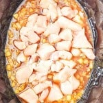 Raw diced chicken pieces in a Crock Pot with corn and liquid, ready to be cooked into flavorful Crock Pot Hawaiian Chicken.