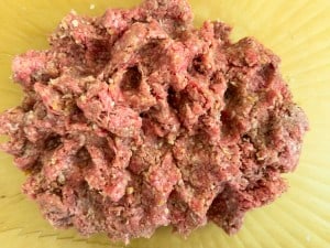 A mound of raw ground beef mixed with seasoning sits on a yellow surface, ready to transform into savory slow cooker Salisbury steak.